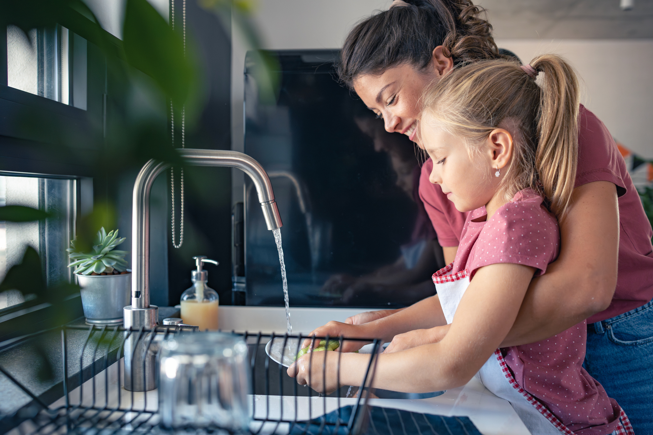 A cute little girl helps her mother wash dishes